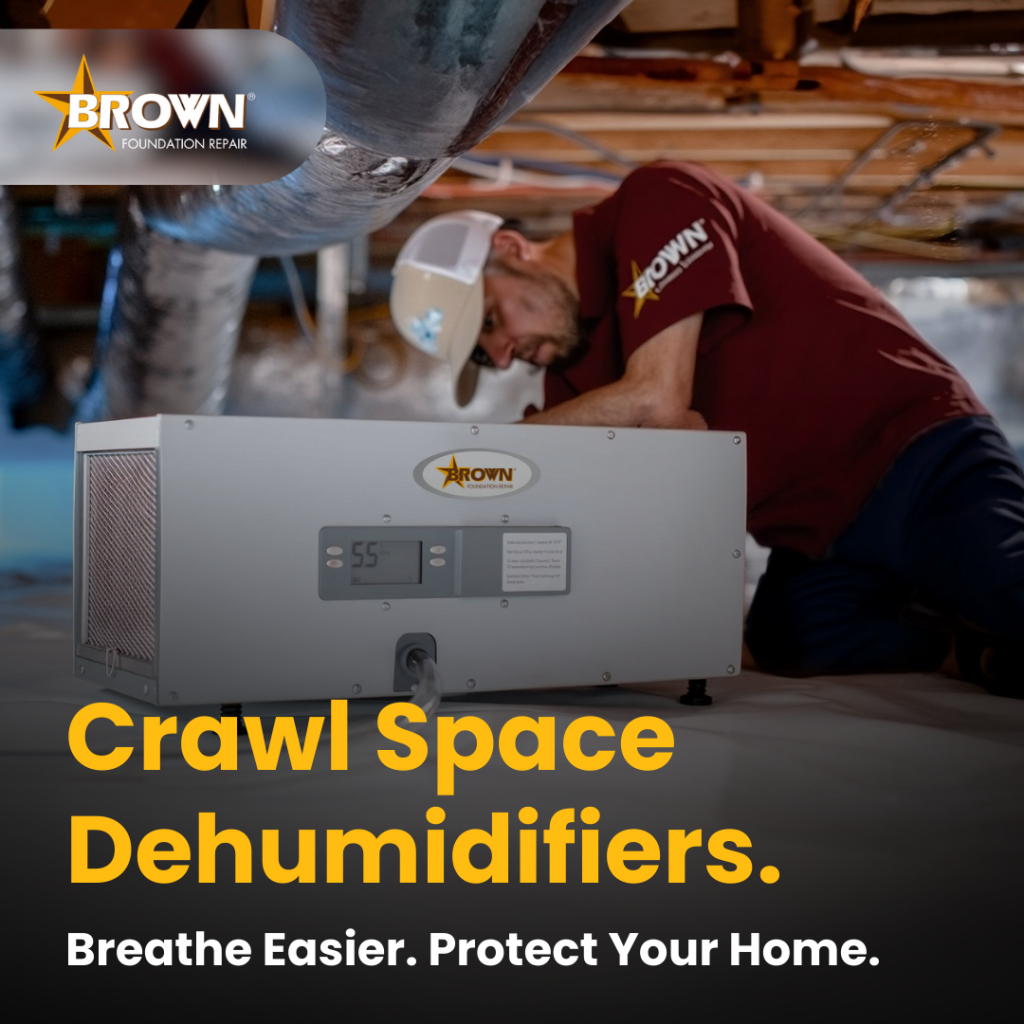 Technician installing a crawl space dehumidifier from Brown Foundation Repair under a home to control moisture and improve air quality.